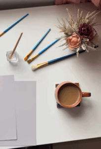 painting supplies on white desk with latte